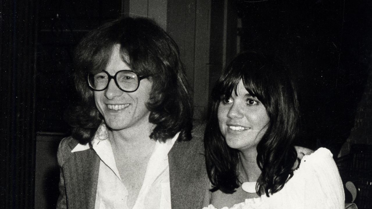 a man with long hair and glasses next to a woman